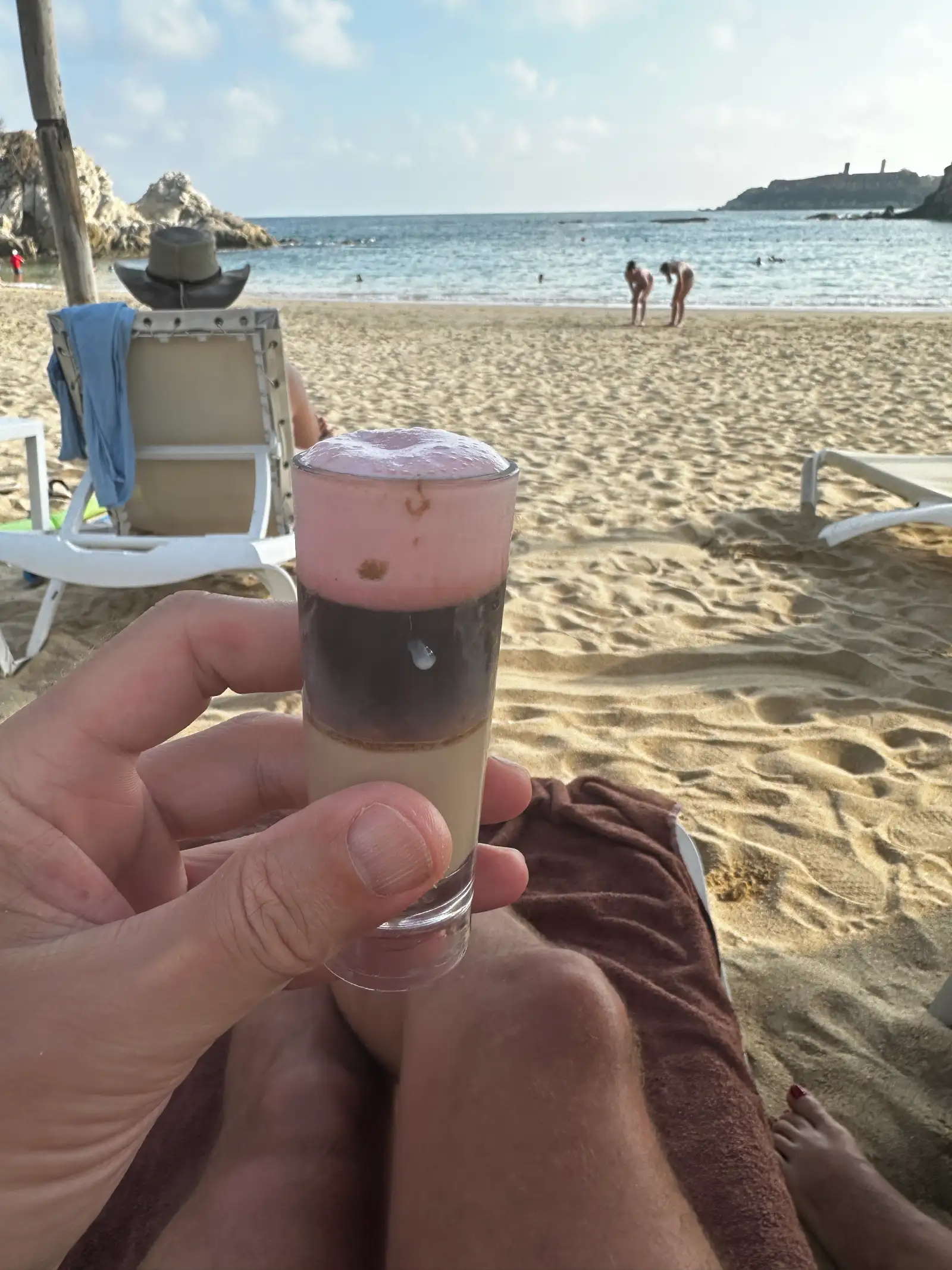 Behind the shades holding a pink lady shooter on the beach.